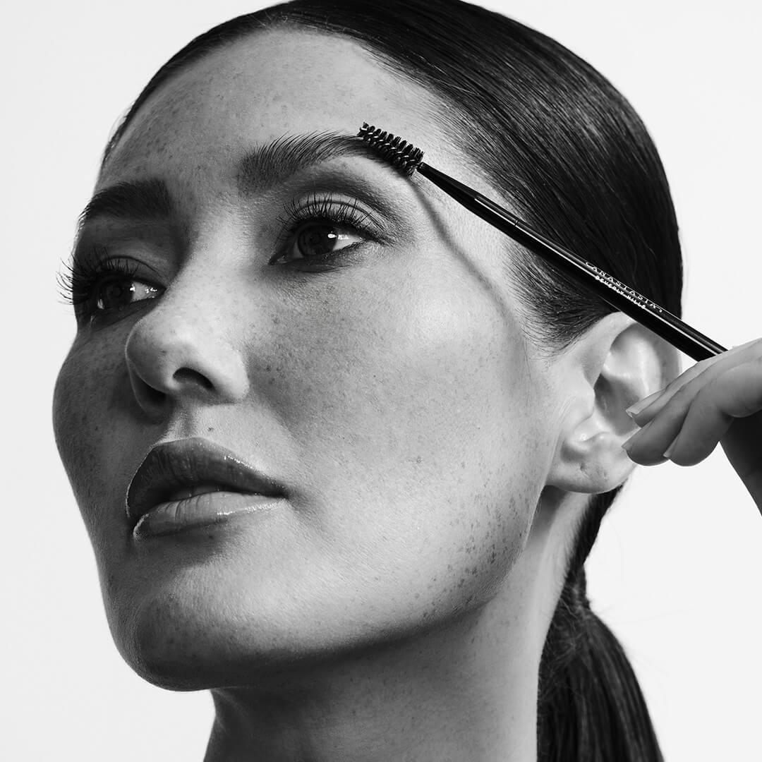 Black and white portrait of a beautiful model fixing her brow with a spoolie Mobile