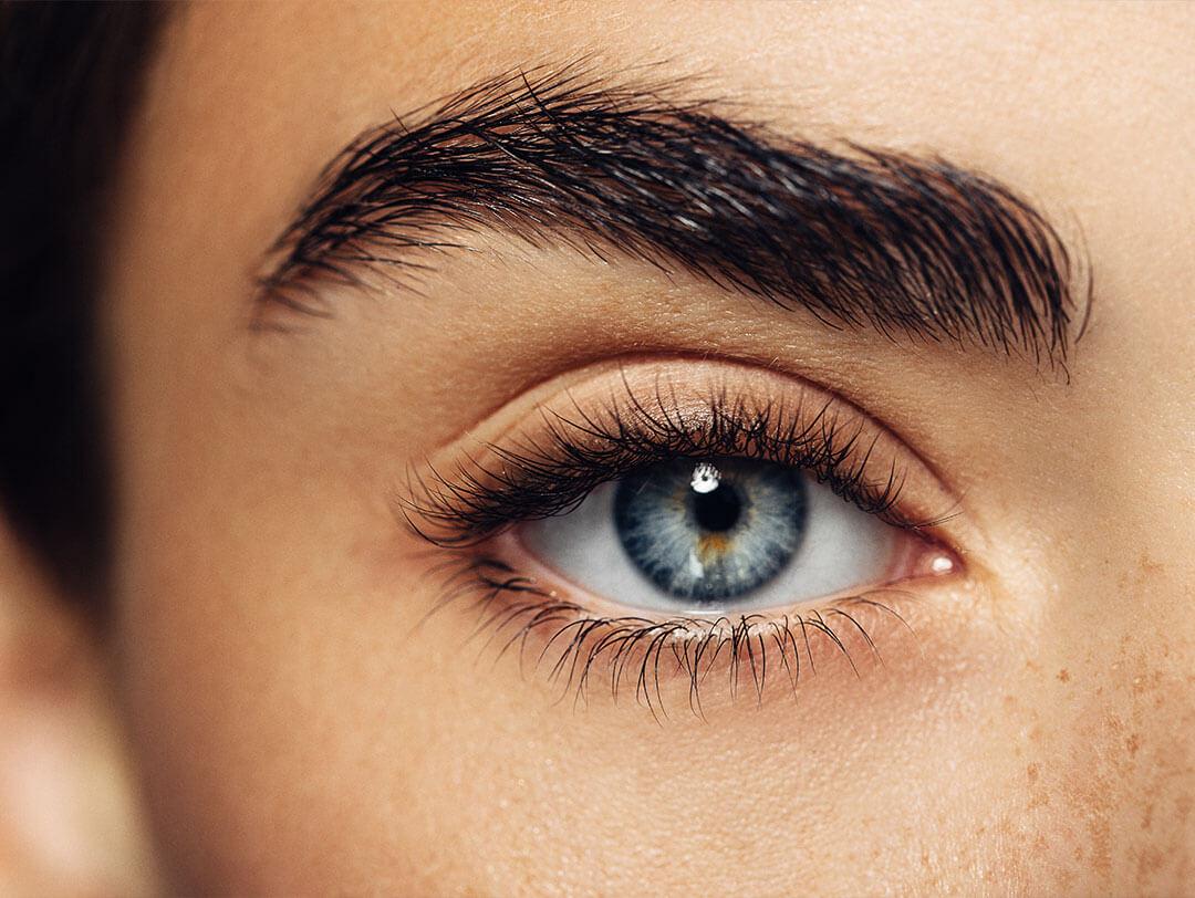 A beautiful woman with fair skin, thick brows, and blue eyes wearing clump-free mascara Desktop