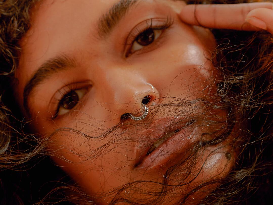 A closeup photo of a model with curly hair and a nose pricing