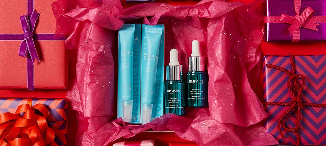 Flat lay image of two tubes of TULA SKINCARE Go Away Acne Spot Treatment, two bottles of 111SKIN 3 Phase Anti Blemish Booster, and colorful gift boxes Desktop