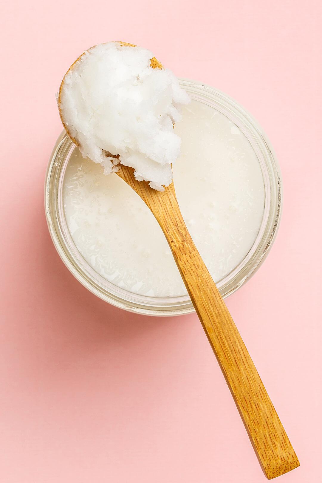 Jar of coconut oil with wooden spoon on pink background Desktop