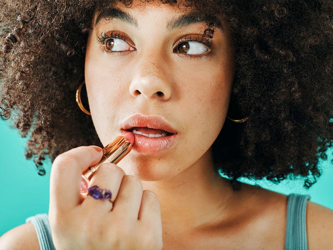 A close-up image of a curly-haired girl applying lipstick Desktop
