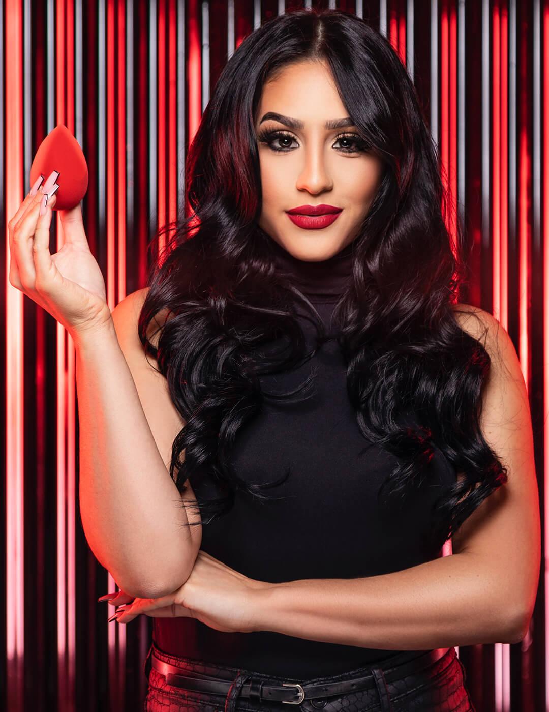 Tricia Hernandez holding a beauty sponge and posing against corrugated metal sheet Desktop