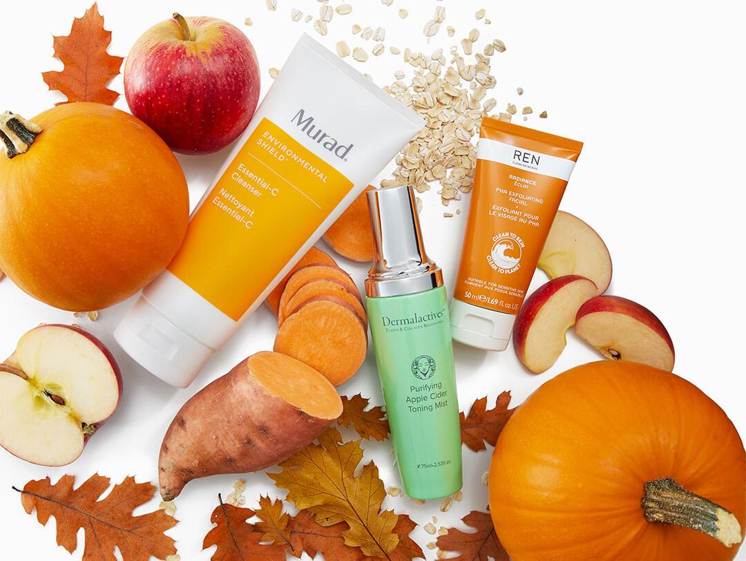 Various skincare products scattered across white background surrounded by fall leaves, apples, pumplins, and sweet potato Desktop
