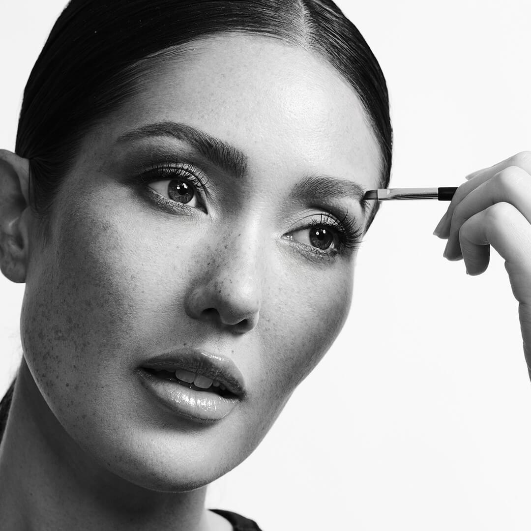 Black and white portrait of a beautiful model applying brow product with a brush Mobile