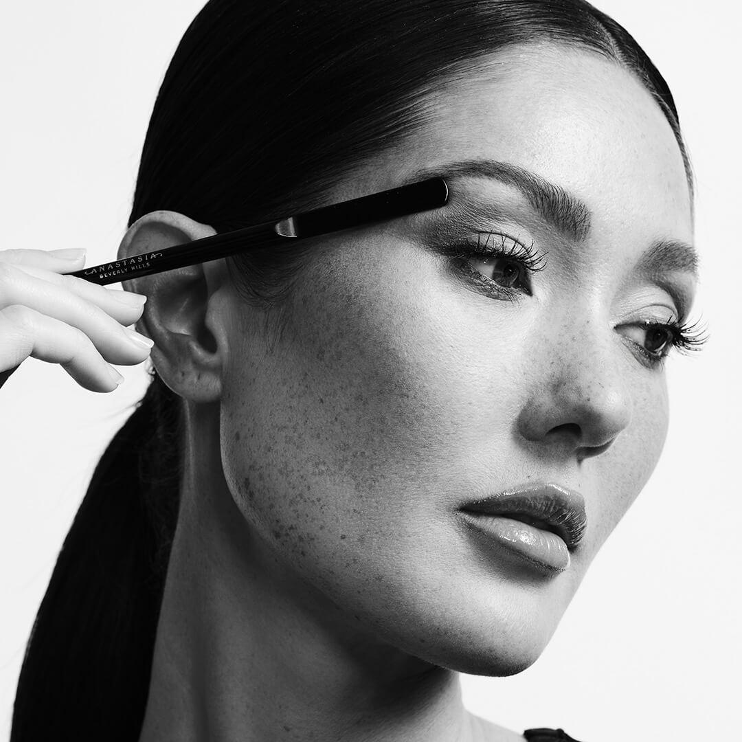 Black and white portrait of a beautiful model holding a brow pencil to her temple Mobile