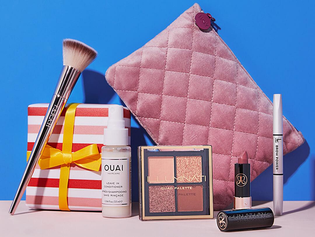 Flat-lay image of beauty products, pink stripes gift box, and rose quilted makeup pouch on blue background