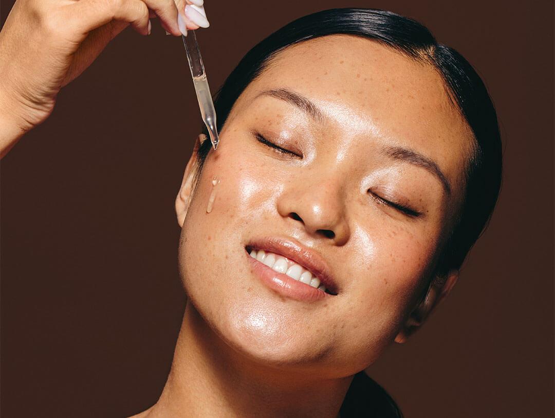 Woman with olive skin indulges in skincare routine using facial serum