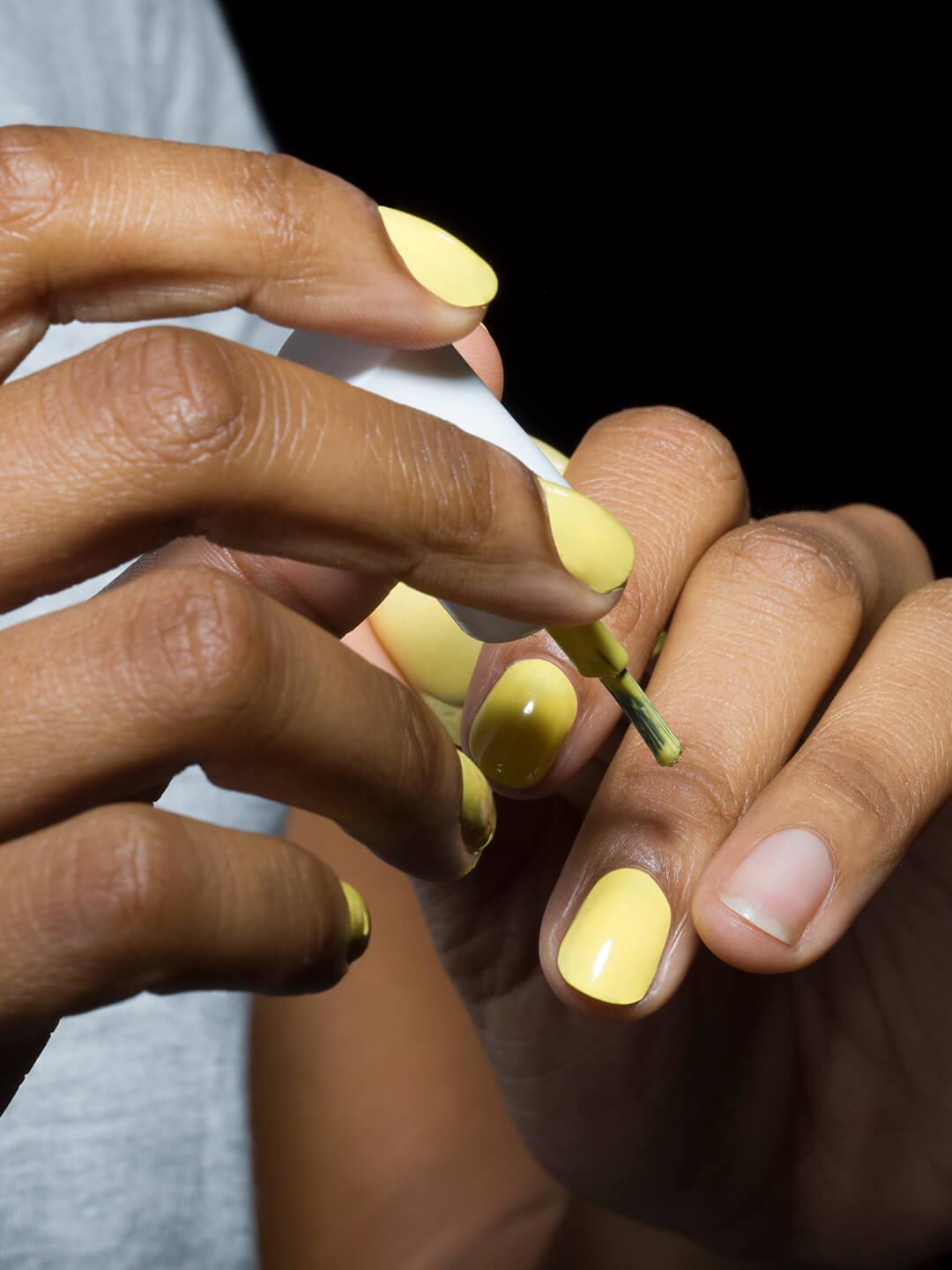 Close-up of young mixed-race woman applying yellow nail polish